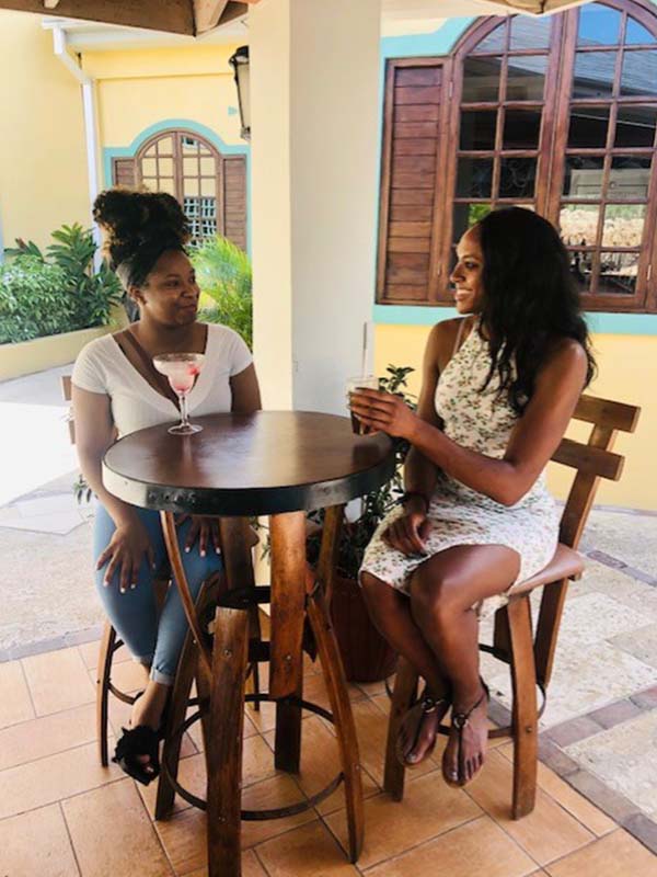 Two African American Women Smiling While Sitting Sipping Cocktails